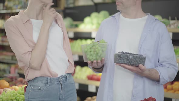 Unrecognizable Caucasian Couple Choosing Grapes in Grocery. Smiling Man Holding Green and Blue