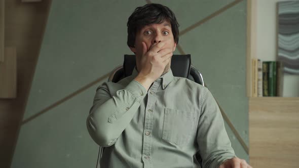 Young Man with a Surprised Expression is Sitting in a Chair in the Office