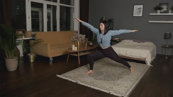 Young Asian Woman Doing Yoga Exercises in her Cozy Dark Room at Home in the Evening
