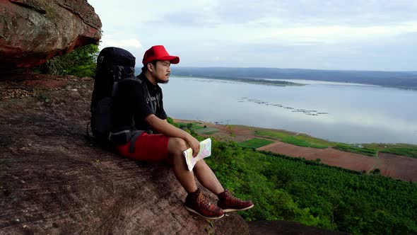 man traveler with backpack sitting on the edge of cliff, on a top of the rock mountain