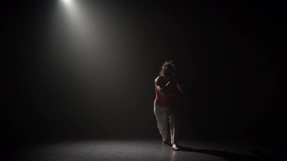 Female Practicing Capoeira in Darkness Under Spotlight in Studio