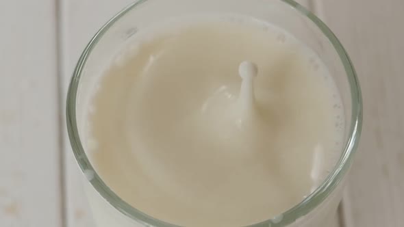 Closeup of Milk Drops Falling Into a Full Glass of Milk on a Light Surface