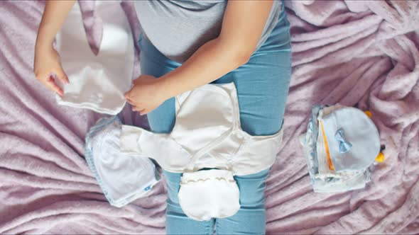 A pregnant woman with a large belly considers baby clothes for the unborn child. Top view of a pregn