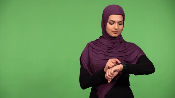 A Young Beautiful Muslim Woman Works on a Smartwatch with a Smile  Green Screen Background