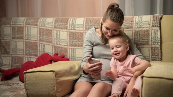 A young pregnant woman and her little daughter make video calls to relatives