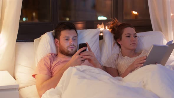 Couple with Smartphone and Book in Bed at Night 40