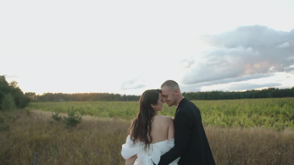 The Newlyweds Stand in Nature with Their Heads Bowed to Each Other and the Groom Kisses the Bride