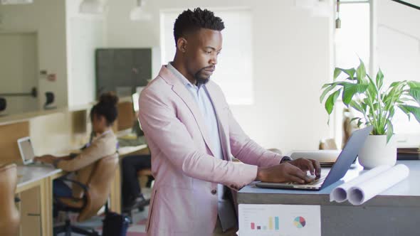 African american businessman using laptop with colleagues in creative office