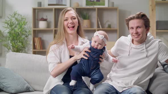 Happy Mother and Father with Baby Daughter Sitting on Sofa at Home