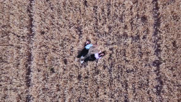 Aerial view of two women waving hands to drone camera while laying on the floor at a wheat field