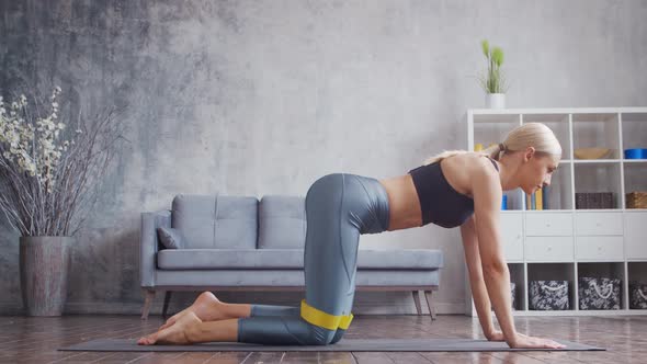 Young and sporty girl in sportswear is doing exercises in home interior using resistance band.