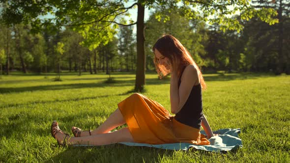 Happy Smiling Attractive Woman Sitting on Green Grass and Have Conversation Via Digital Smartphone