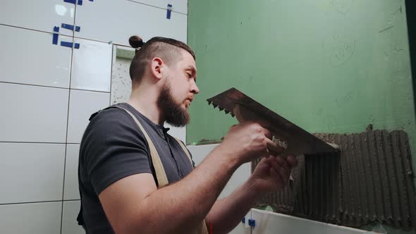 Repairman Applying Tile Adhesive with a Notched Trowel on the Bathroom Wall