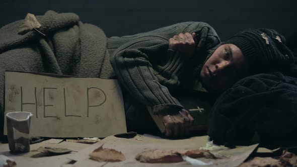 Crying Homeless Person With Bible and Help Sign on Cardboard Lying on Floor