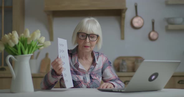 Senior Female Teacher in Glasses Talks and Shows Sheet of Paper with Simple Mathematical Equations