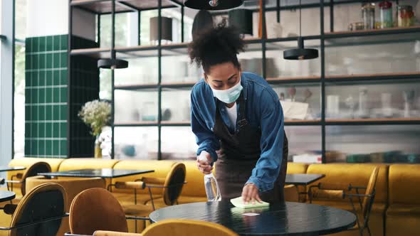 A african american cafe worker woman wearing protective medical mask cleaning the table