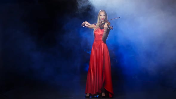 Girl in a Red Dress Playing the Violin. Studio. Smoke