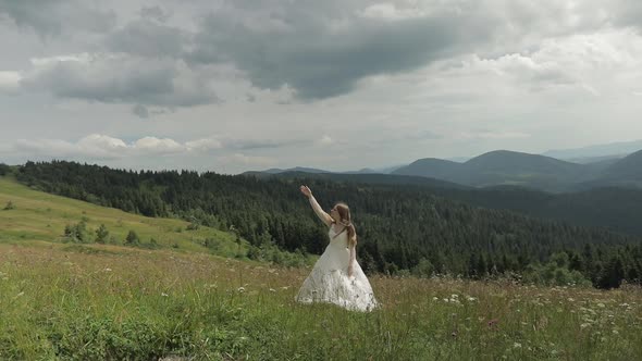 Beautiful Bride in Wedding Dress Stay on the Mountains. Raises Her Hand Up