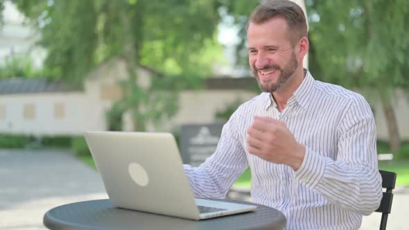 Successful Middle Aged Man Celebrating on Laptop in Outdoor Cafe