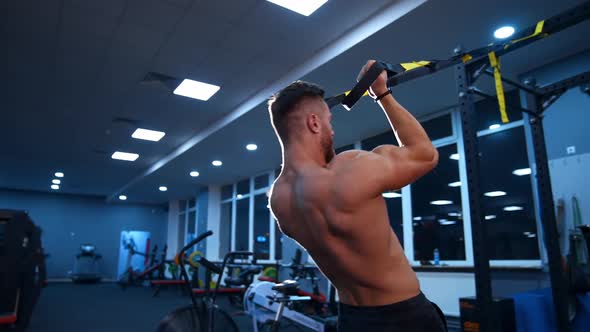 Handsome athlete trains with ropes in gym.