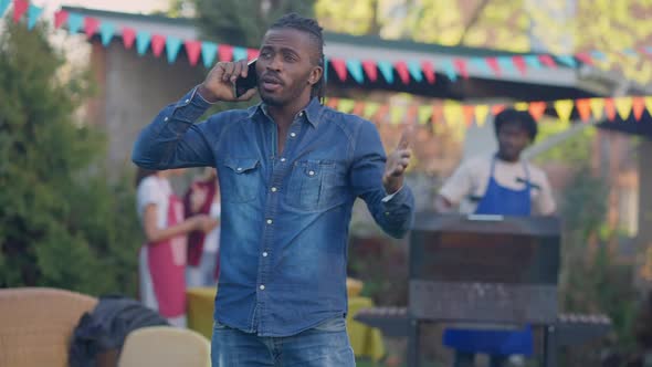 Busy Serious African American Man Talking on the Phone Discussing Business with Blurred Friends