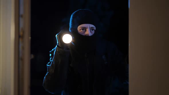 Medium Shot Portrait of Caucasian Thief with Flashlight Looking Inside Open House Entering Leaving