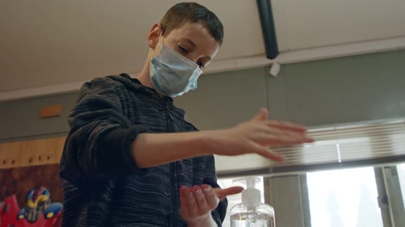 Corona pandemic boy with face mask using hand sanitizer to prevent coronavirus