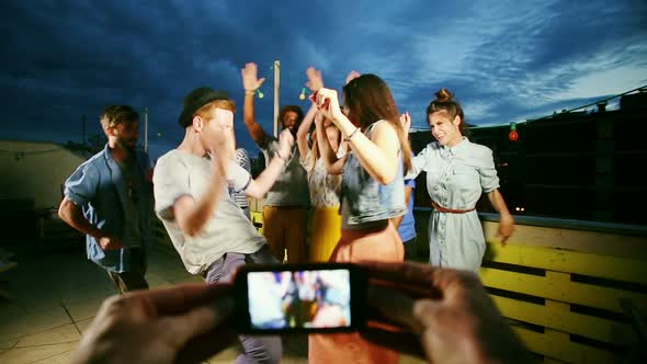 View of hands filming couple dancing in the middle and friends around them