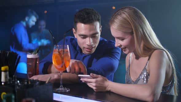 Dating Couple Using Phone Sitting at Bar Counter