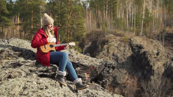 Caucasian Woman Sits on Rock and Plays the Ukulele