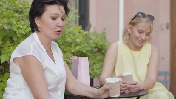 Portrait of Two Relaxed Carefree Women Chatting with Someone in Outdoor Cafe and Laughing. Positive