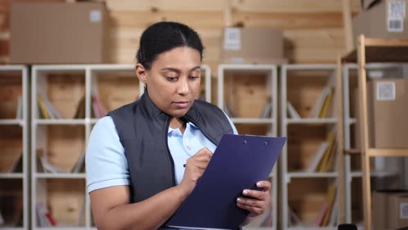 Attentive Black Female Post Office Employee Filling out Checklist