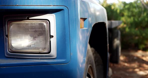 Slide right along the headlight and side of an old vintage blue cargo truck with tires parked on a d