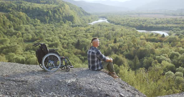 Disabled Man Sitting on the Stone on the Top of the Hill and Breathing on Full