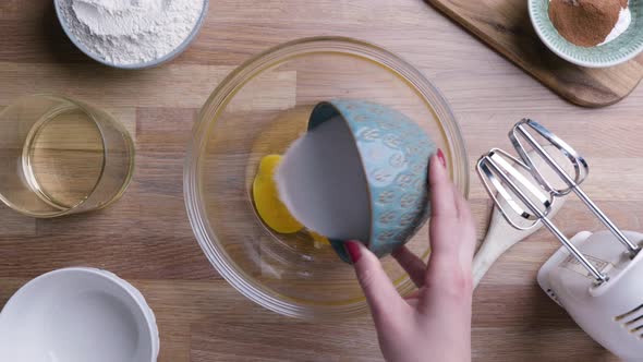 Adding A Cup Of White Sugar To Fresh Eggs In A Bowl. overhead shot