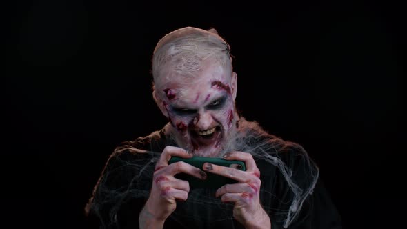 Sinister Man Halloween Zombie Enthusiastically Playing Racing Drive Video Games on Mobile Phone