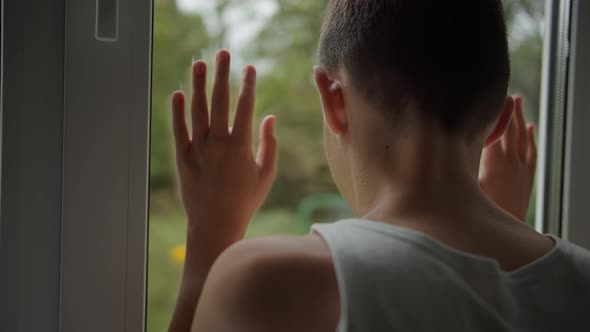 Sad Boy Sitting Inside and Looking Out the Window, Misses Someone