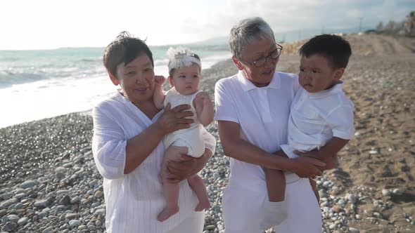 Smiling Asian Grandmothers Holding Grandchildren on Hands Standing on Mediterranean Sea Coast at