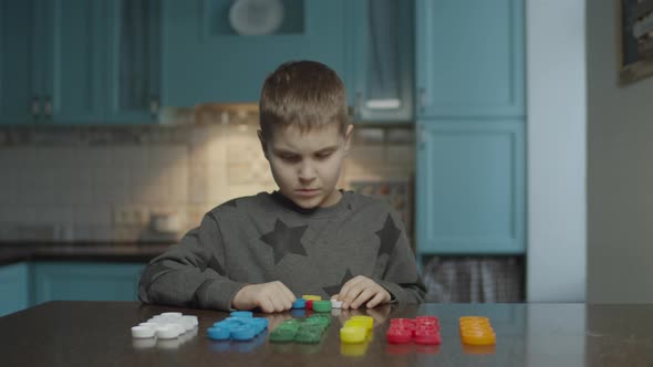 Autistic Boy Sorting Plastic Caps By Colors on the Table at Home. Kid with Autism Sorting Color Caps