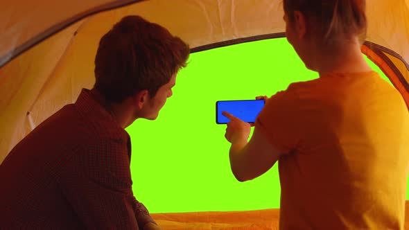 Woman and Man are Sitting in Tent and Looking at Phone with Green Screen