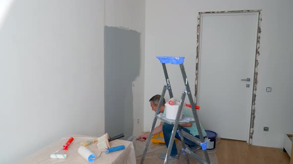 A Man in a Shirt Paints the Walls with a Roller Gray