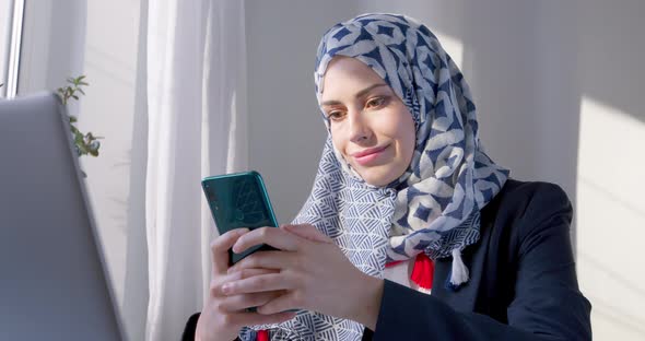 Arab woman uses a smartphone. Muslim young woman in hijab holds a mobile phone. 4K.