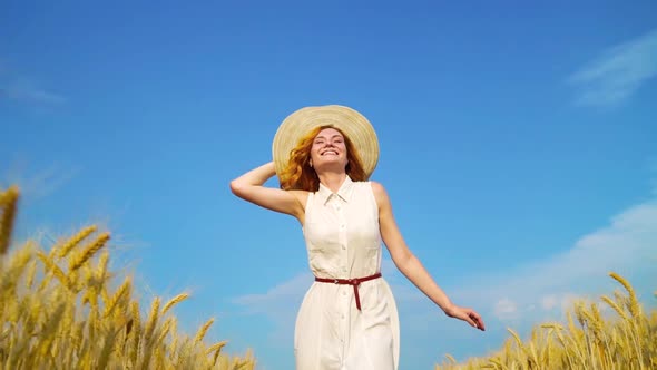 Pretty Smiling Red Haired Woman Walking in Wheat Field with Blue Sky on Background