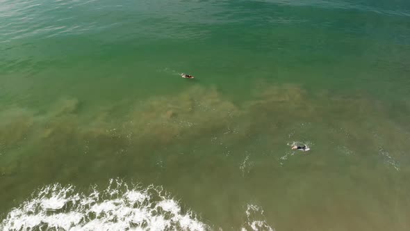 Aerial shot of two surfers paddling to catch a wave.