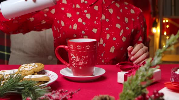 Woman in Red Pajamas with a New Years Print Decorates a Cup of Hot Drink with Whipped Cream