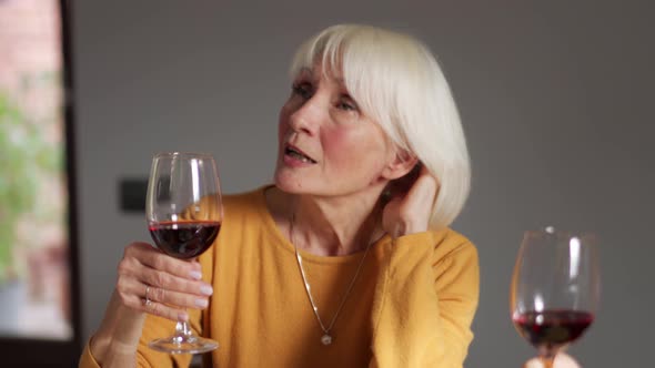 Pensive blond mature woman talking with glass of wine