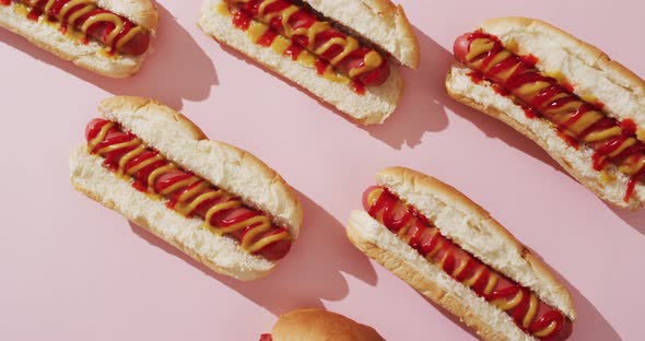 Video of hot dogs with mustard and ketchup on a pink surface