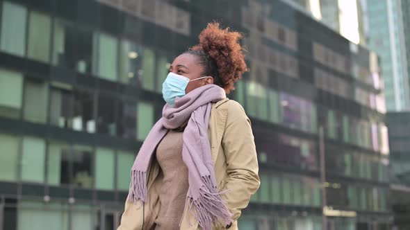 Young black woman putting on medical mask and then taking off against cityscape