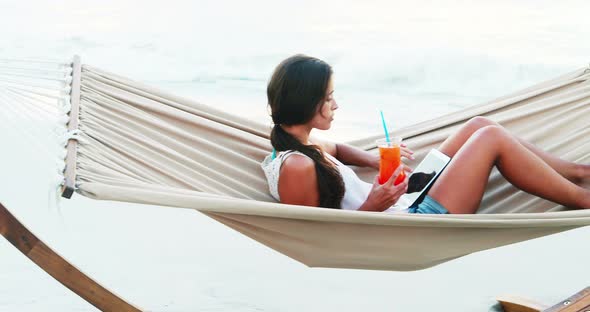 Woman relaxing on hammock and using digital tablet