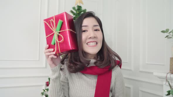 Asian woman holding christmas gifts smiling to camera in her living room.